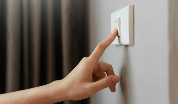 pessoa mostra como economizar energia elétrica ao desligar o interruptor de luz em parede branca
