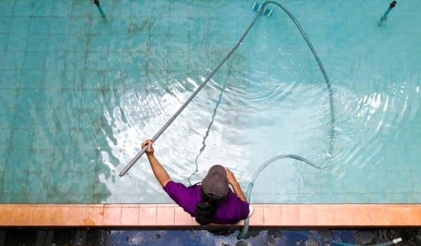 qual é o melhor cloro para piscina - pessoa fazendo limpeza em piscina