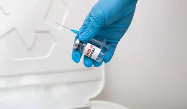 Mão com luva azul descarta frasco de vacina e seringa utilizados no lixo infectante