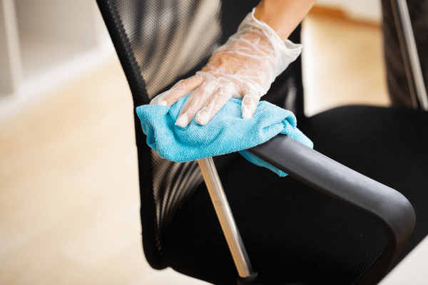 Profissional de luva transparente higienizando o braço de uma cadeira com um pano azul 