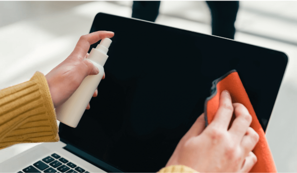 Profissional limpando a tela do seu notebook com pano e spray de água no escritório.