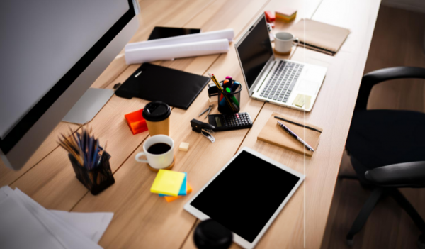 Mesa de escritório em madeira com materiais de escritório para empresas como notebook, monitor blocos autoadesivos, lápis, canetas, marcadores e folhas sulfite. 