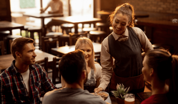 Atendente de restaurante servindo uma mesa de clientes com seus respectivos pedidos